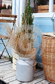 Wicker basket Near bouquet of dried flowers on wooden porch. Cozy Decor of terrace of country house.