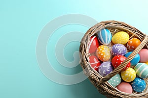 Wicker basket with painted Easter eggs on color background, top view.