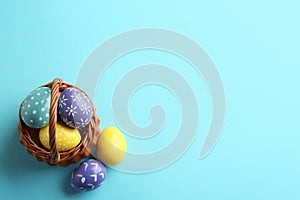 Wicker basket with painted Easter eggs on color background, top view.