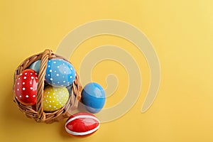 Wicker basket with painted Easter eggs on color background, top view