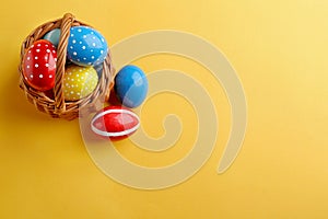 Wicker basket with painted Easter eggs on color background, top view.