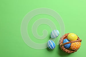 Wicker basket with painted Easter eggs on color background, top view