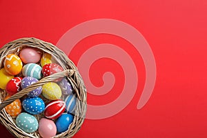 Wicker basket with painted Easter eggs on color background, top view