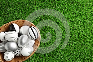 Wicker basket of painted Easter eggs on green lawn, top view