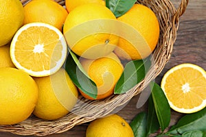 Wicker basket, ripe juicy oranges and green leaves on wooden table, flat lay