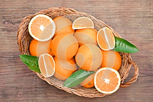 Wicker basket with ripe juicy oranges and green leaves on wooden table, top view