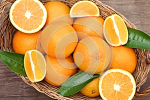 Wicker basket with ripe juicy oranges and green leaves on wooden table, top view