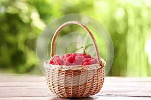 Wicker basket with ripe raspberry on wooden table against blurred background