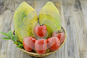 Wicker basket with sweet papaya and ripe persimmon on wooden table