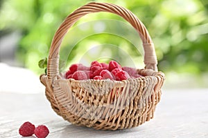 Wicker basket with sweet ripe raspberries on table outdoors