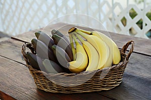 Wicker basket with tasty purple and yellow bananas on wooden table