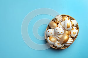 Wicker basket of traditional Easter eggs decorated with golden paint on color background, top view