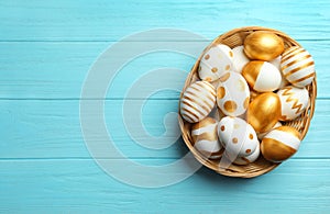 Wicker basket of traditional Easter eggs decorated with golden paint on wooden background, top view.