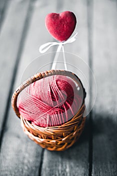 Wicker basket on a wooden background with a ball of threads and hearts