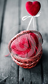 Wicker basket on a wooden background with a ball of threads and hearts