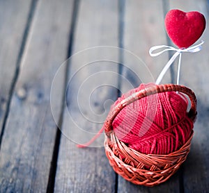 Wicker basket on a wooden background with a ball of threads and hearts