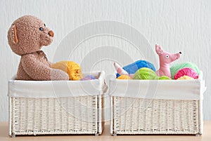 Wicker baskets with balls of knitting yarn and funny toys on table against light background