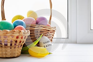 Wicker baskets with bright colorful eggs and with text Happy Easter and flower