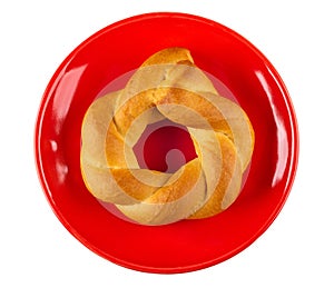 Wicker bun in shape ring in red saucer isolated on white. Top view