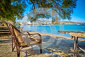 Wicker chair by seafront under pine tree on beach on sunny day. Holidays, relax, vacations, summer, Milos island, Greece