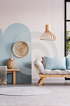 Wicker chandelier above wooden Scandinavian sofa with futon in bright living room interior photo