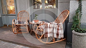 Wicker cozy armchair with blanket and small glass table outdoors. Plaid lies on the wicker furniture from rattan.