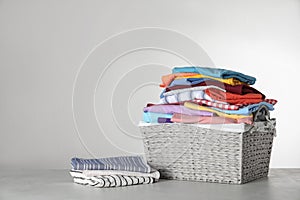 Wicker laundry basket with clean clothes on table against light background