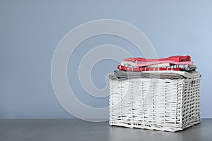 Wicker laundry basket with clean towels on table against color background