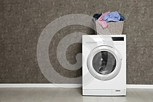 Wicker laundry basket full of dirty clothes on washing machine near color wall