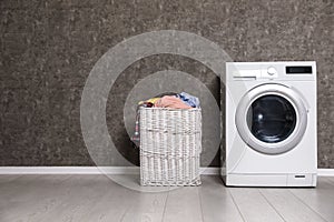 Wicker laundry basket full of dirty clothes and washing machine near color wall