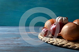 Wicker mat with garlic and onions on color wooden table