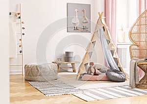 Wicker peacock chair next to tent with pillows and pouf in scandinavian designed girl`s playroom, real photo