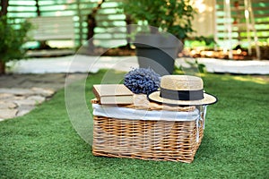 Wicker picnic basket  with flowers on grass in garden. Weekend concept. Picnic basket with a book and a bouquet of lavender on the