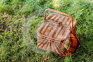 Wicker picnic basket with rug on green grass