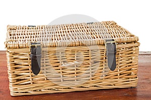 Wicker picnic basket sitting on mahogany wood table.