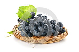 Wicker plate with ripe sweet grapes on white background