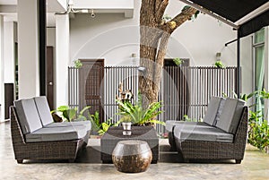 Wicker sofa with pillows and table standing on garden terrace by the house