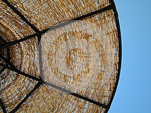 The wicker sun umbrella on the blue sky background. Detail