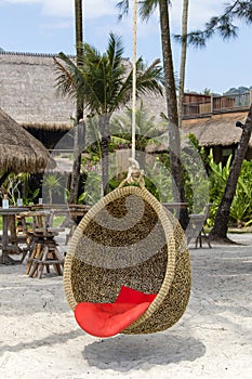 Wicker swing with a pillow hanging on a coconut palm next to the sea on the sand beach. Island Koh Kood, Thailand