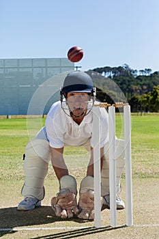 Wicketkeeper looking at ball crouching behind stumps on field