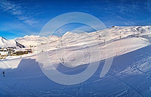 Wide aerial panorama of snowy mountain ridge on winter sunrise. Stunning mountains range covered with snow powder on ski