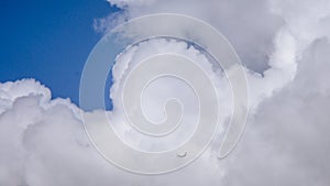 Wide aerial shot of an airplane high above in white clouds in a blue sky