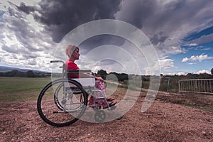 Wide angle disabled girl sitting in a wheelchair in the middle of a green field in the countryside with a sky clouds