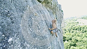 Wide angle handheld camera young strong man rock climber climbing on a vertical limestone cliff, attaching rope and