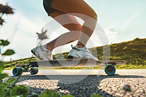 Wide angle legs on a skateboar or longboard in motion at sunny day on the asphalt road. Close up of a spinning wheel.
