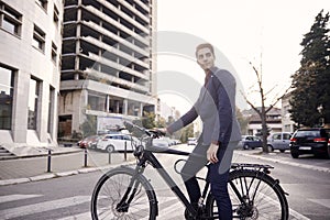 Wide angle lens shot of city street buildings and cars, one man posing, sitting on bicycle outdoors. 20-29 years old, wearing suit