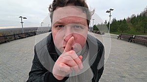 Wide angle lens: young fat man looking at camera and showing silence gesture. Finger on lips