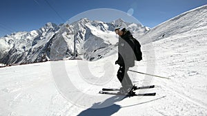 A wide angle male skier aged in black equipment and white helmet with ski poles rides on a snowy slope on a sunny day