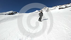 A wide angle male skier aged in black equipment and white helmet with ski poles rides on a snowy slope on a sunny day