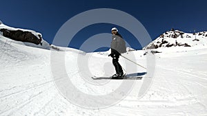 A wide angle male skier aged in black equipment and white helmet with ski poles rides on a snowy slope on a sunny day